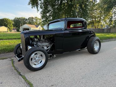 Sleek black vintage hot rod with exposed engine and polished wheels.