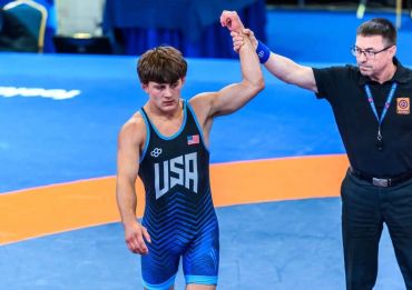 Wrestler in USA singlet has his hand raised in victory.
