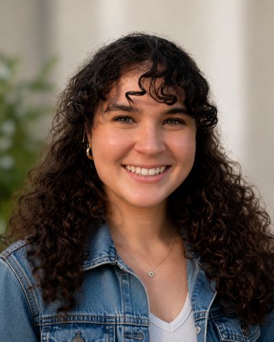 Smiling young woman with curly hair in a denim jacket.