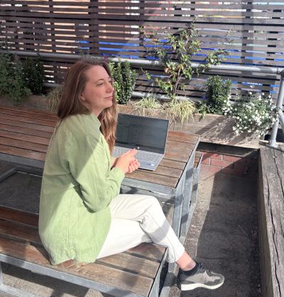 A woman sitting outdoors with a laptop, enjoying the sunlight.