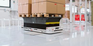 Automated guided vehicle transporting pallets with boxes in a clean warehouse.