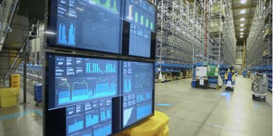 Warehouse with digital monitoring screens and automated robots managing inventory.