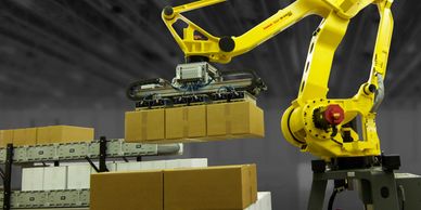Yellow robotic arm stacking boxes on a pallet in a warehouse.
