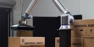 Robotic arm handling boxes labeled Universal Robots in an industrial setting.