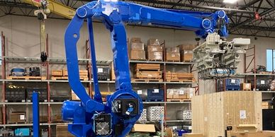 A large blue industrial robotic arm in a warehouse handling equipment.
