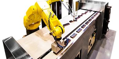 Yellow industrial robotic arms assembling products on a conveyor belt.