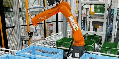 An orange robotic arm operating in a factory with blue and green crates.