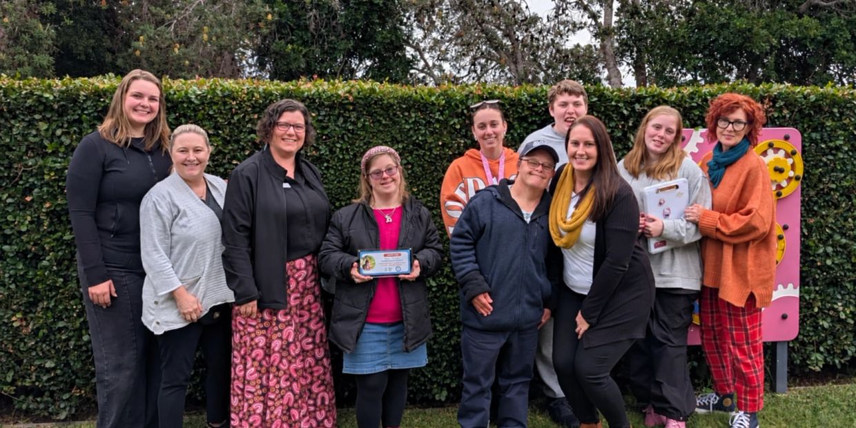 Group of people smiling outdoors in front of a hedge.