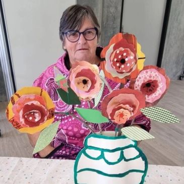 Elderly woman with handmade paper flowers in a vase.