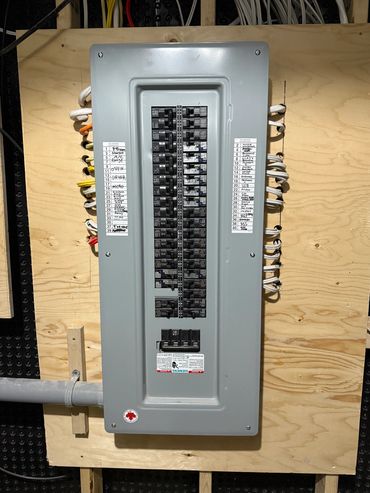 Residential electrical panel with labeled circuit breakers mounted on plywood.