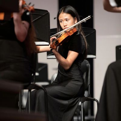 Young woman focused on playing violin during a concert.