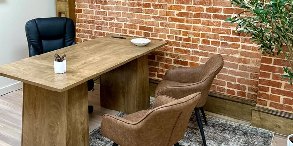 Modern office setup with wooden desk, leather chairs, and exposed brick wall.