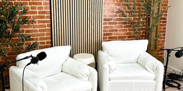 Two white armchairs with microphones set up for recording against a brick wall.