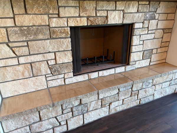 A stone fireplace with a tiled hearth and a metal grate inside.