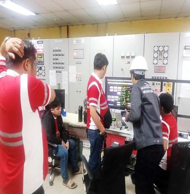 Workers monitoring control panels and screens in an industrial control room.