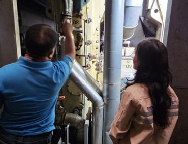 Two workers inspect industrial machinery in a factory setting.