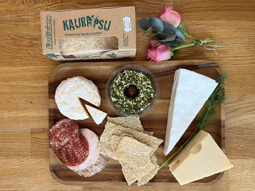 A charcuterie board with cheeses, crackers, meats, and herbs on a wooden table.