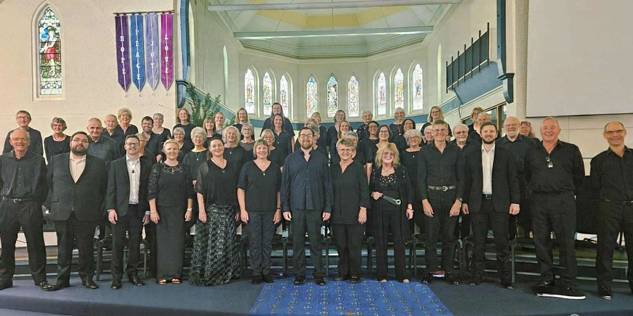 Large choir group posing in a church with stained glass windows.