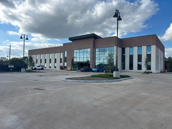 Modern office building with large windows and a spacious parking lot under a partly cloudy sky.