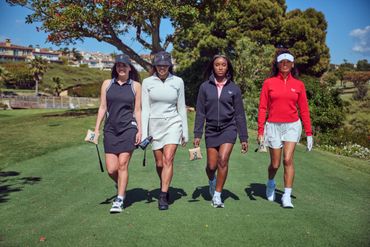 Four women walking confidently on a golf course in stylish golf attire.