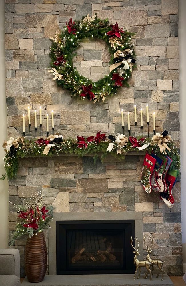 Stone fireplace decorated with festive holiday wreath, garland, stockings, candles, and golden reindeer.
