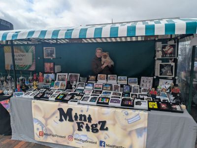 A market stall selling Mini FigZ collectible displays with a person and dog behind the table.