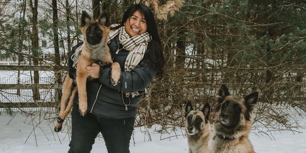 Woman joyfully holding a puppy with two other dogs sitting in the snow.