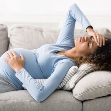 Pregnant woman resting on couch, looking unwell.