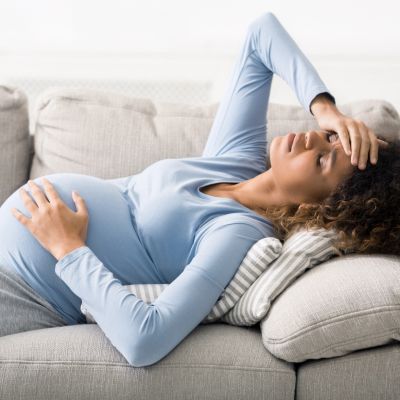 Pregnant woman lying on couch, feeling discomfort.
