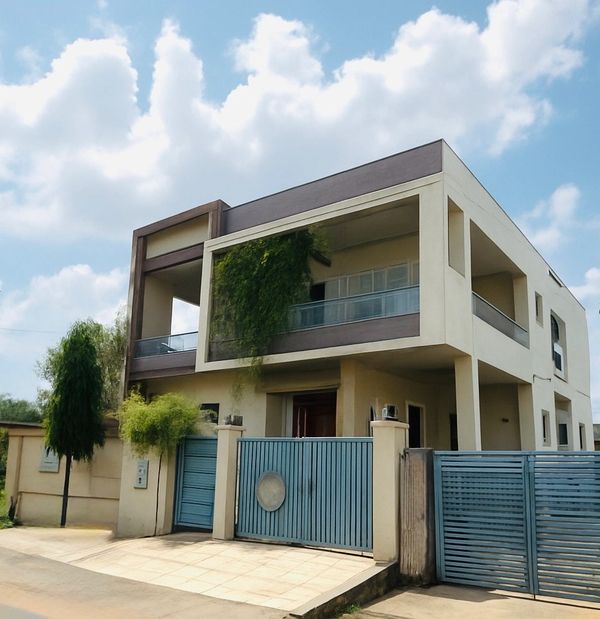 Modern two-story house with blue gates and a balcony covered in greenery.