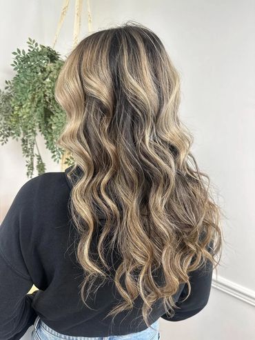 the back of a girls head with wavy hair that just had it wash, cut, styled and colored with blonde