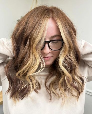a girl with glasses on fluffing up her newly cut, colored and styled haird