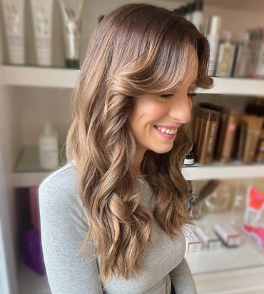 a girl sitting down smiling with a new hair style inside of a hair salon