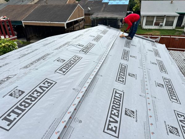 Worker installing roofing underlayment on a house roof.