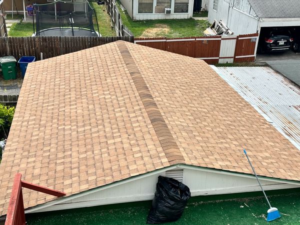 Newly shingled roof on a small building with a broom and black trash bag nearby.