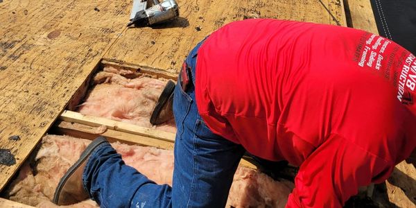 Worker kneeling on roof insulation, preparing for roofing work.