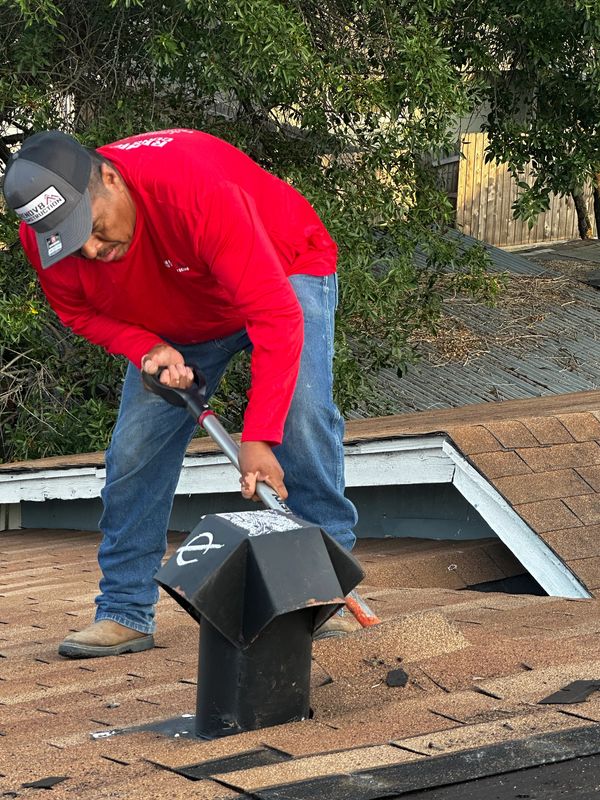 Man in red shirt working on a roof vent with a tool.