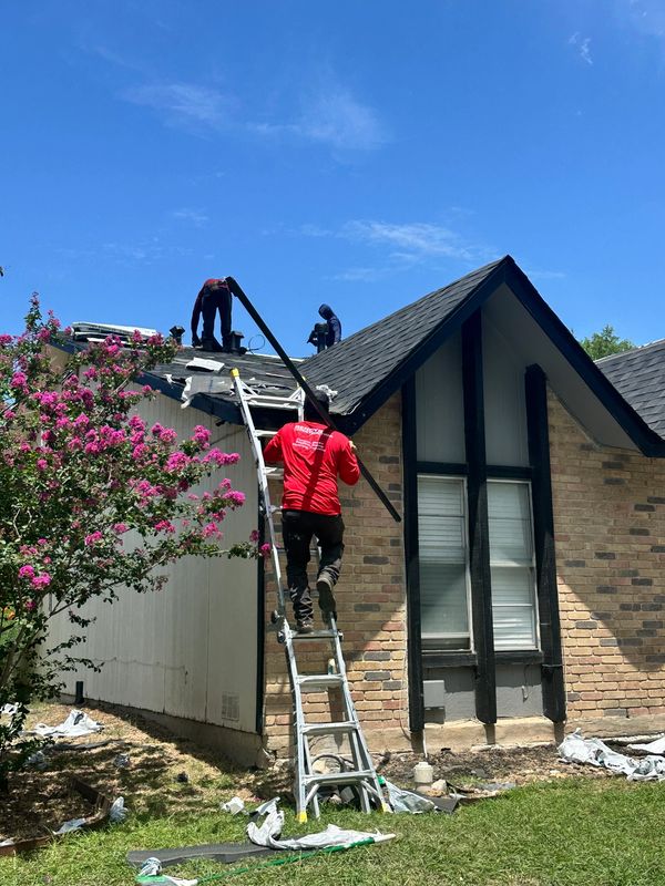 Workers repairing the roof of a brick house on a sunny day.