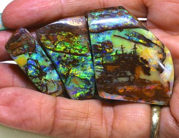 Hand holding three polished, colorful opal stones with vibrant hues.