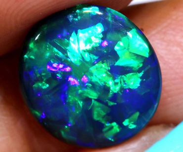 A vibrant blue and green opal gemstone held between fingers.