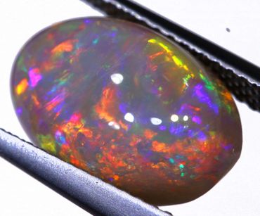 Close-up of a vibrant, multicolored opal gemstone held by tweezers.