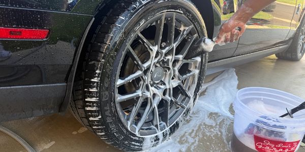 Person washing a car tire with soapy brush and bucket.