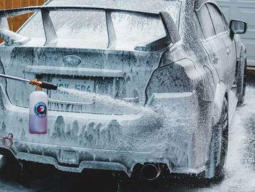 A car being washed with foam and a spray gun.