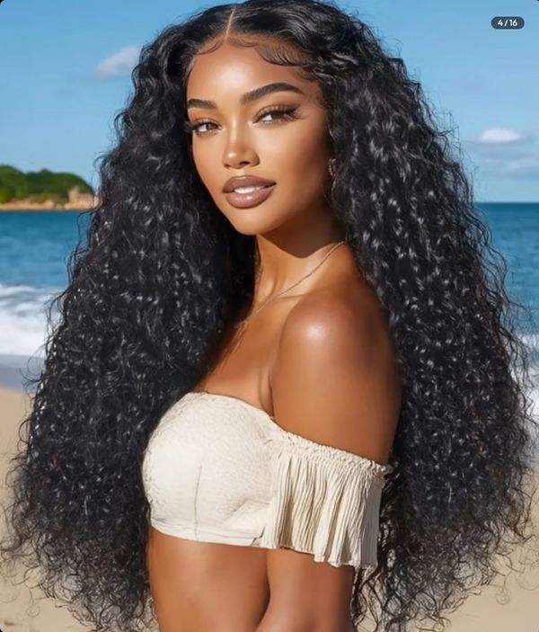 Woman with long curly hair posing on a beach in an off-shoulder top.
