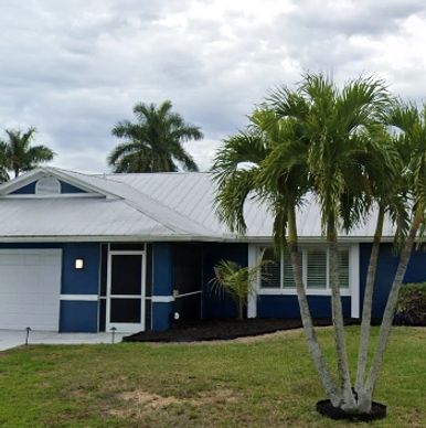 blue painted house with metal roof and palm trees