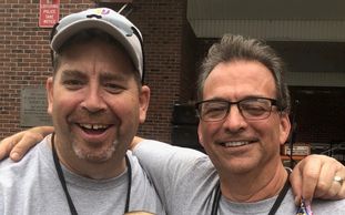 Two men smiling for a selfie outdoors.