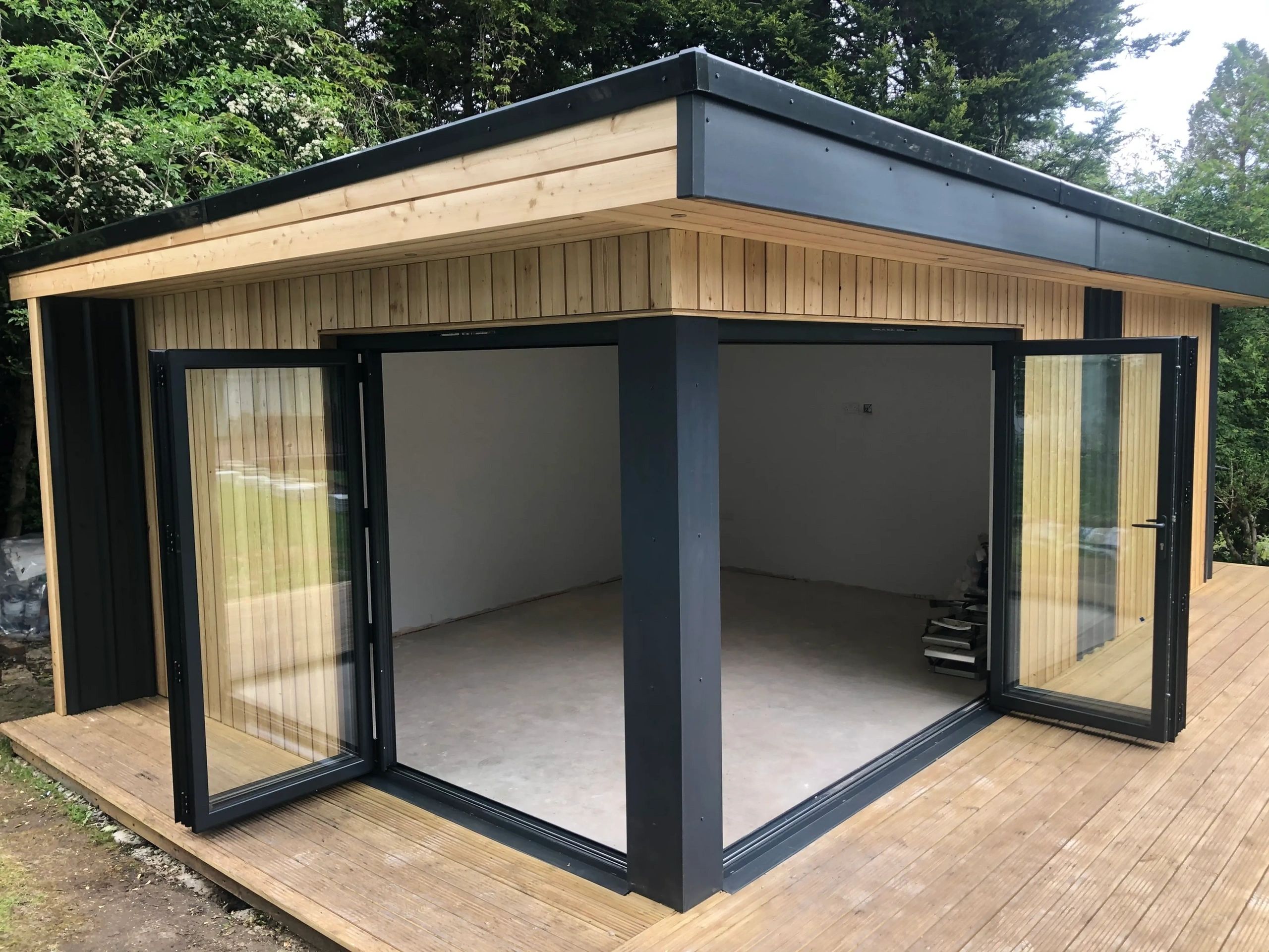 Modern wooden garden room with black-framed open glass doors and a deck.