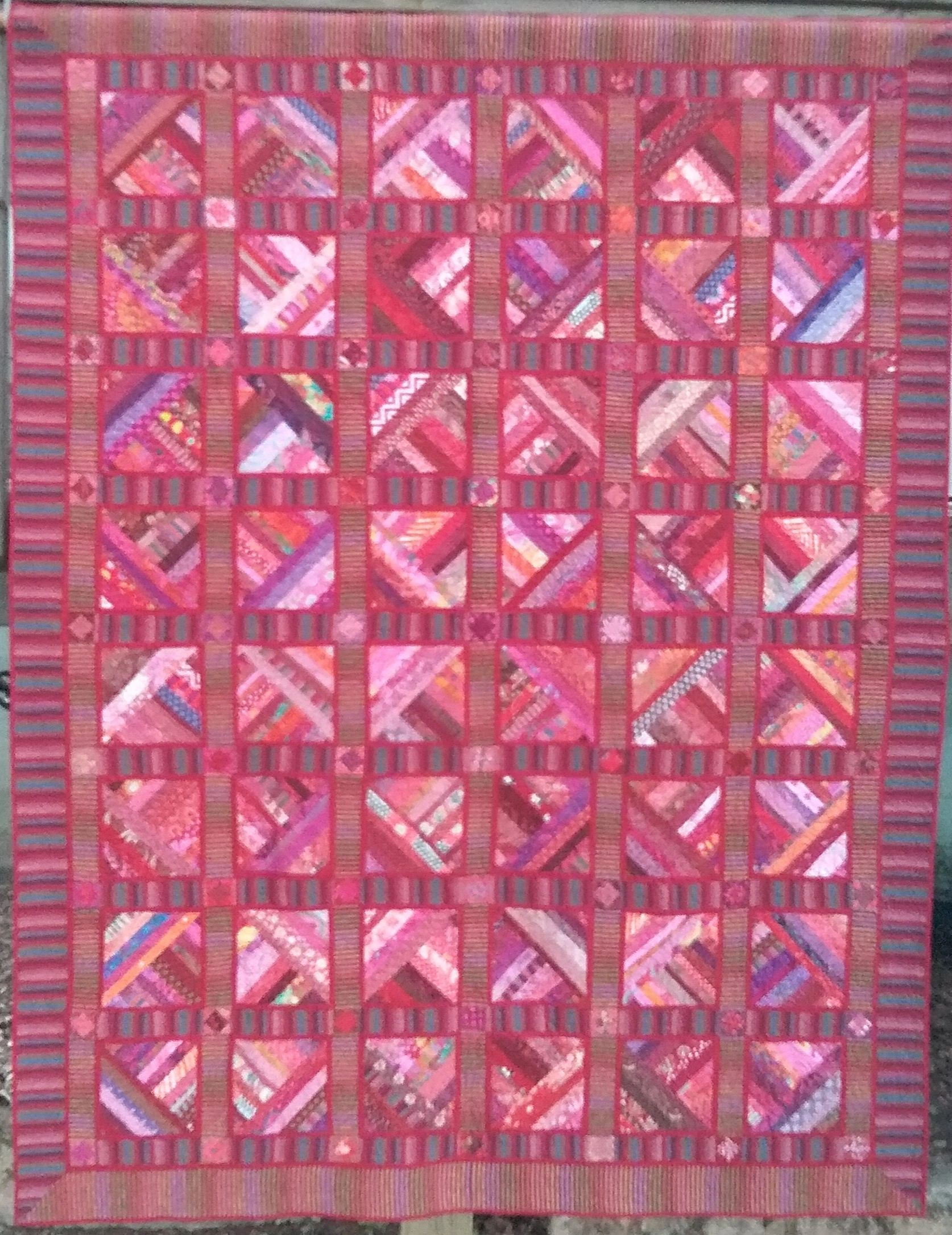 Full size scrappy quilt in pinks and reds, with striped sashing