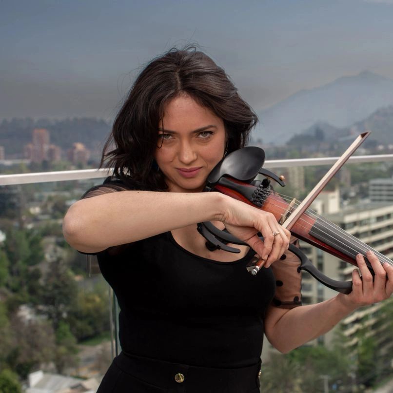 Young woman playing violin on a balcony with a cityscape background.