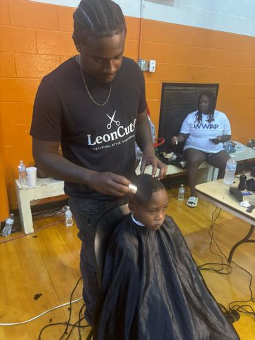A barber carefully styles a young boy's hair indoors.